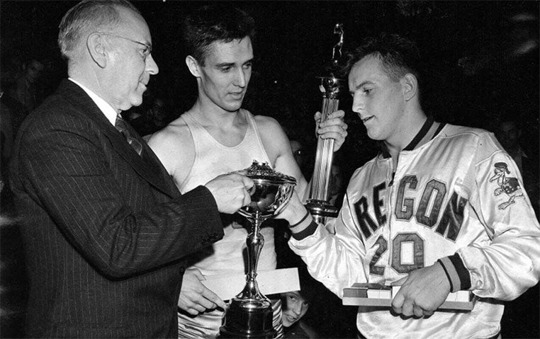 University of Oregon basketball player Bob Anet receiving the 1939 NCAA basketball championship trophy from Big Ten Conference Commissioner John Griffith as Ohio State player James Hull watches.