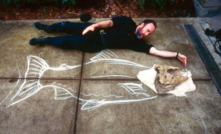 Ray Troll poses with chalk outline of spike-tooth salmon body and skull