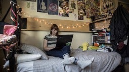 Woman on residence hall bed surfing the web on a laptop
