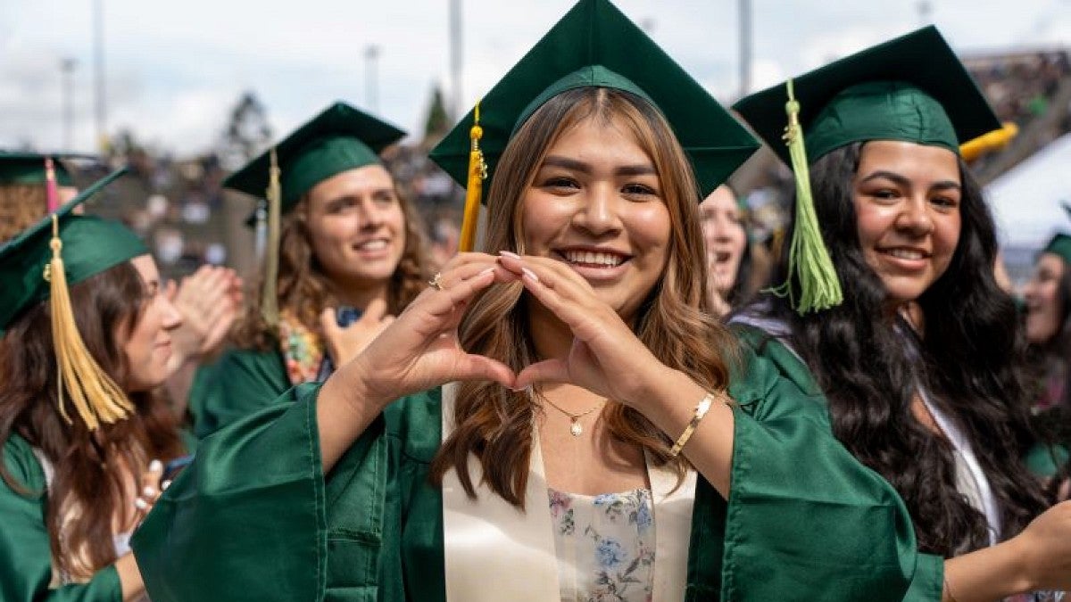 A graduate wearing a green cap and gown throws her O at commencement