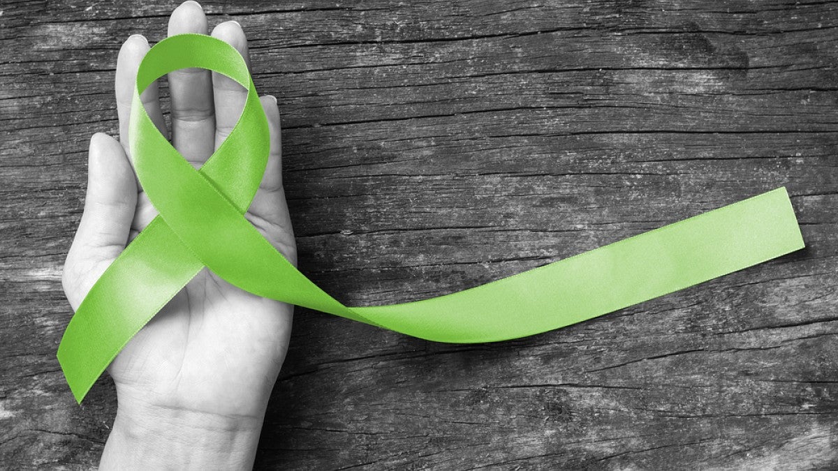 A hand holding a green ribbon, a symbol of mental health.