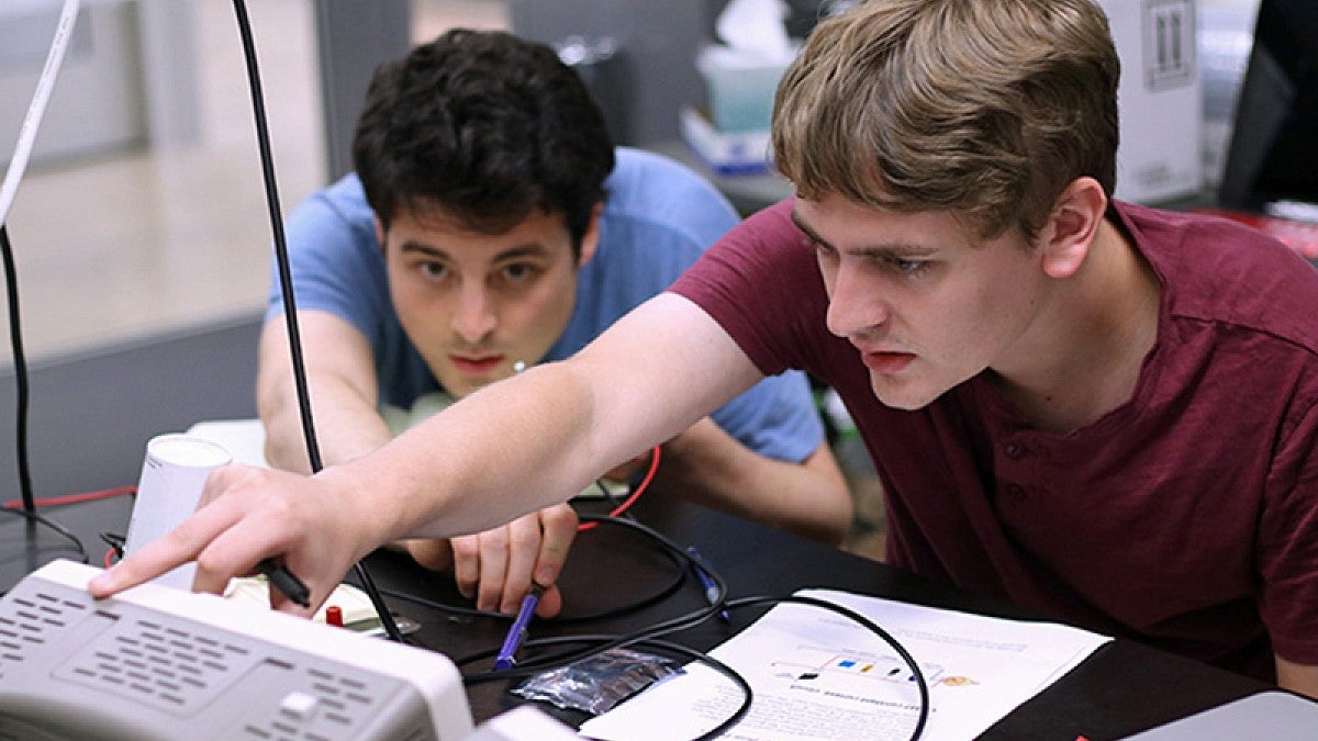 Image shows two students in the internship program at work in a UO optics lab