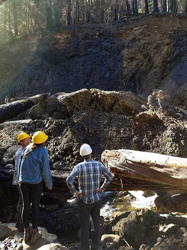 Researchers looking up at a hillside from a rocky river bed