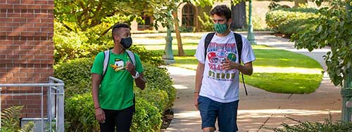 Two students walking through campus wearing masks