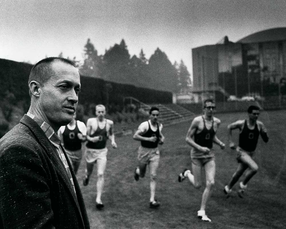 Legendary University of Oregon track coach Bill Bowerman watching as five distance runners, including Phil Knight (second from left), enter a turn on the practice track near Hayward Field in 1959.