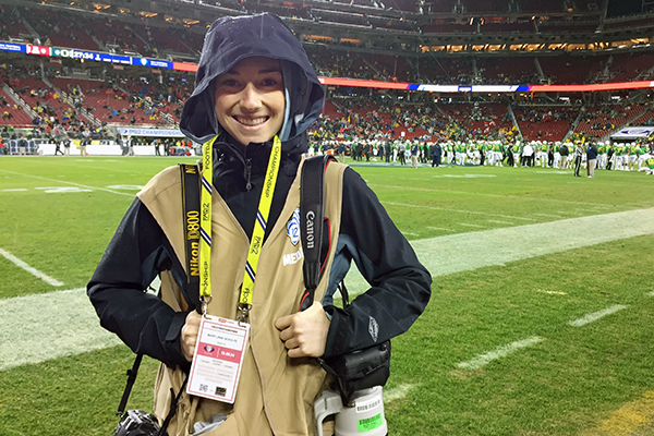 a student journalist poses with lots of gear at a football game