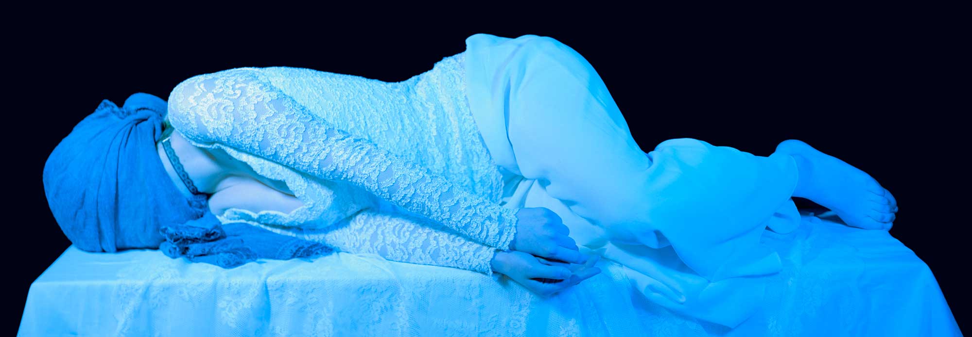 Person covered in a white cloth laying down on a pedestal 