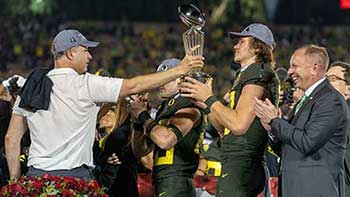 Coach Mario Cristobal handing the Rose Bowl trophy to Justin Herbert on the podium during the postgame celebration