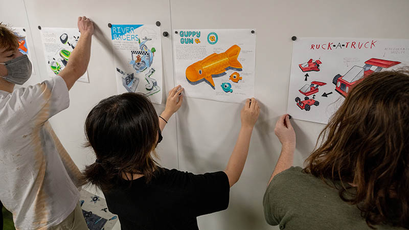 Students in a Product Design class hanging design ideas on a wall during a class review