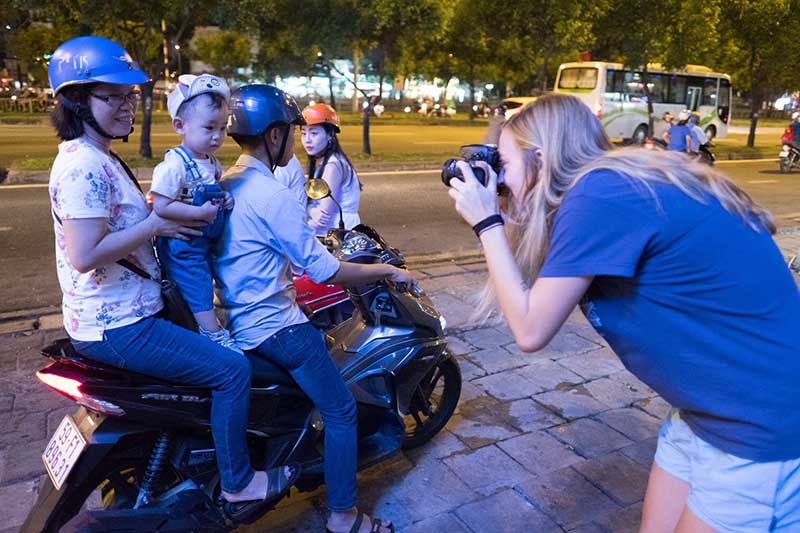 A journalism student takes a photo of a family on a motorcycle