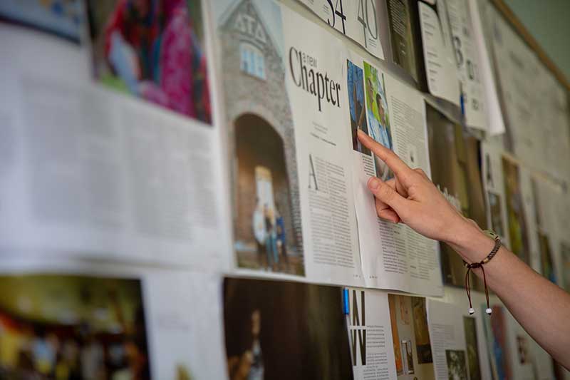Students get practical experience producing Flux magazine. Looking at the pages of the next Flux magazine displayed on a wall.