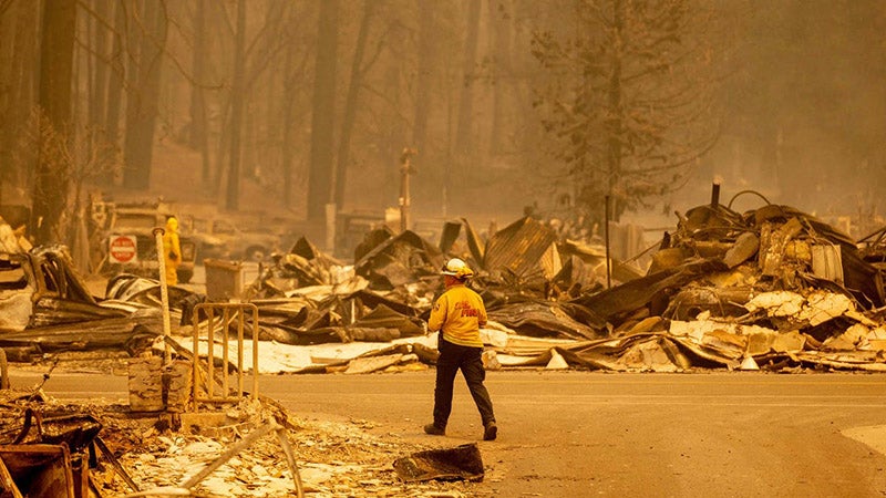 Firefighter walking through a town after a forest fire as seen through a hazy, yellow sky
