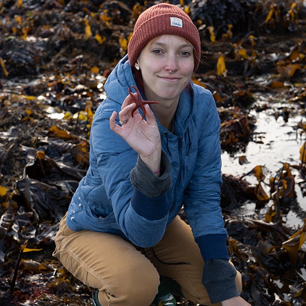Woman in beanie hat and blue coat holding a maroon sea star.