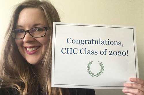 Professor Elizabeth Raisenen with a sign that says Congratulations, CHC class of 2020