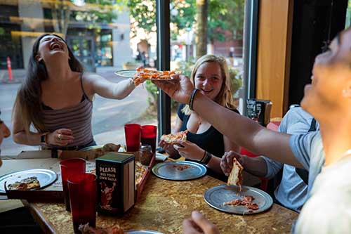 Students laughing while eating pizza