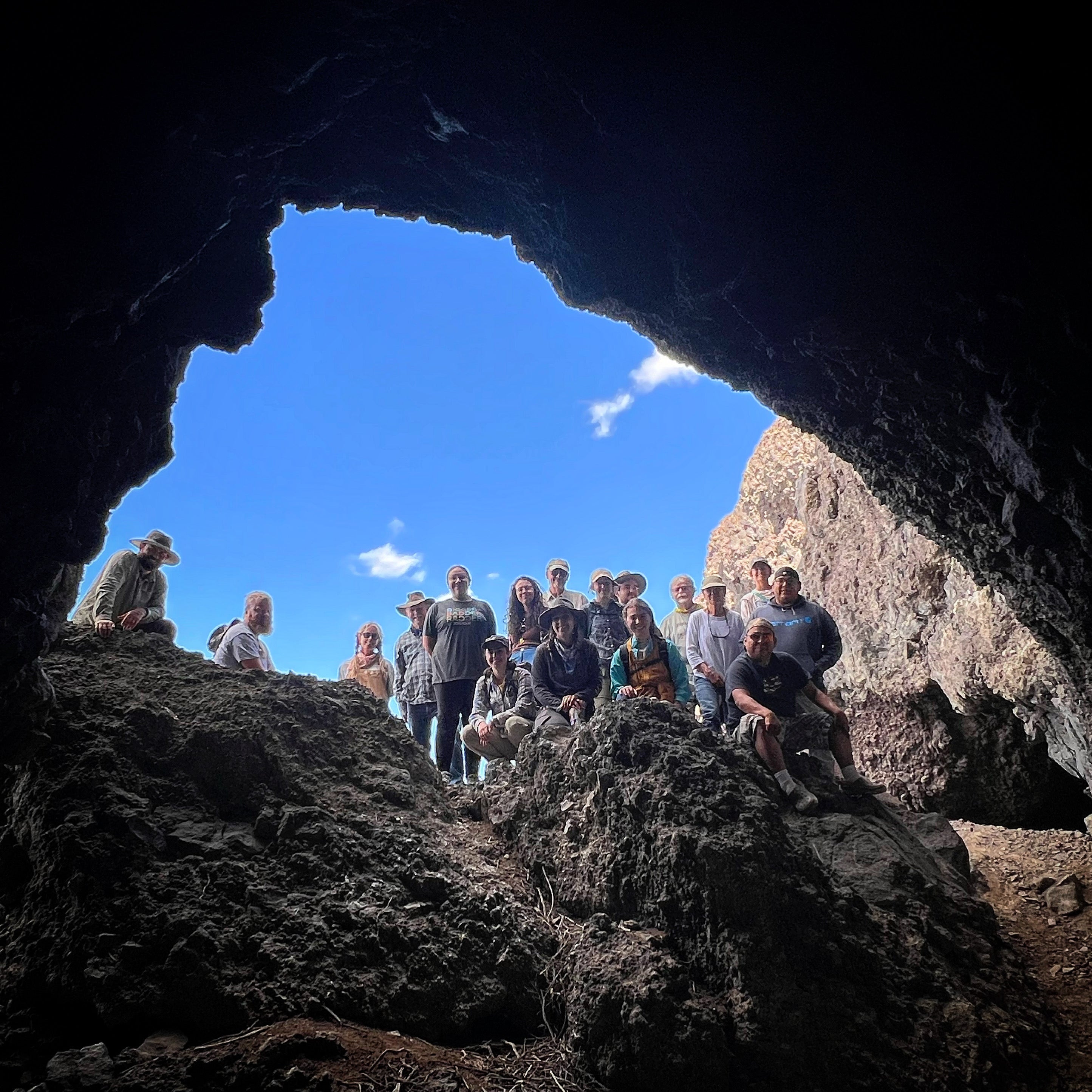 A group of students and staff of field school standing in a cave, largely silhouetted with a blue sky behind.