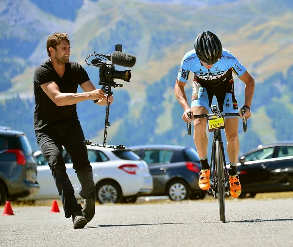 Jake Swantko holds a video camera and runs next to a cyclist who he is filming