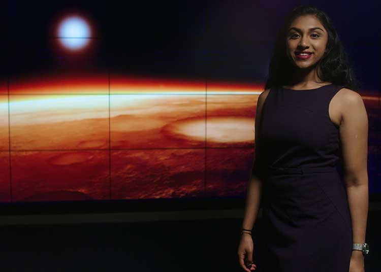 Manju Bangalore in the Price Science Commons Visualization Lab in front of an image of outer space