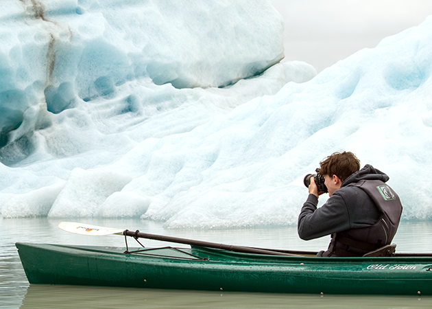 a student shoots photos of a glacier while seated in a kayak