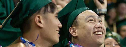 Two students in cap and gown smiling during commencement