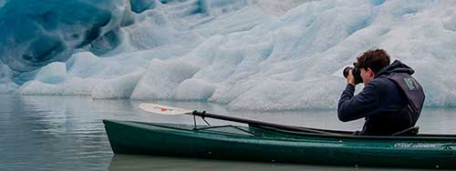Man in a kayak taking a photo of a glacier