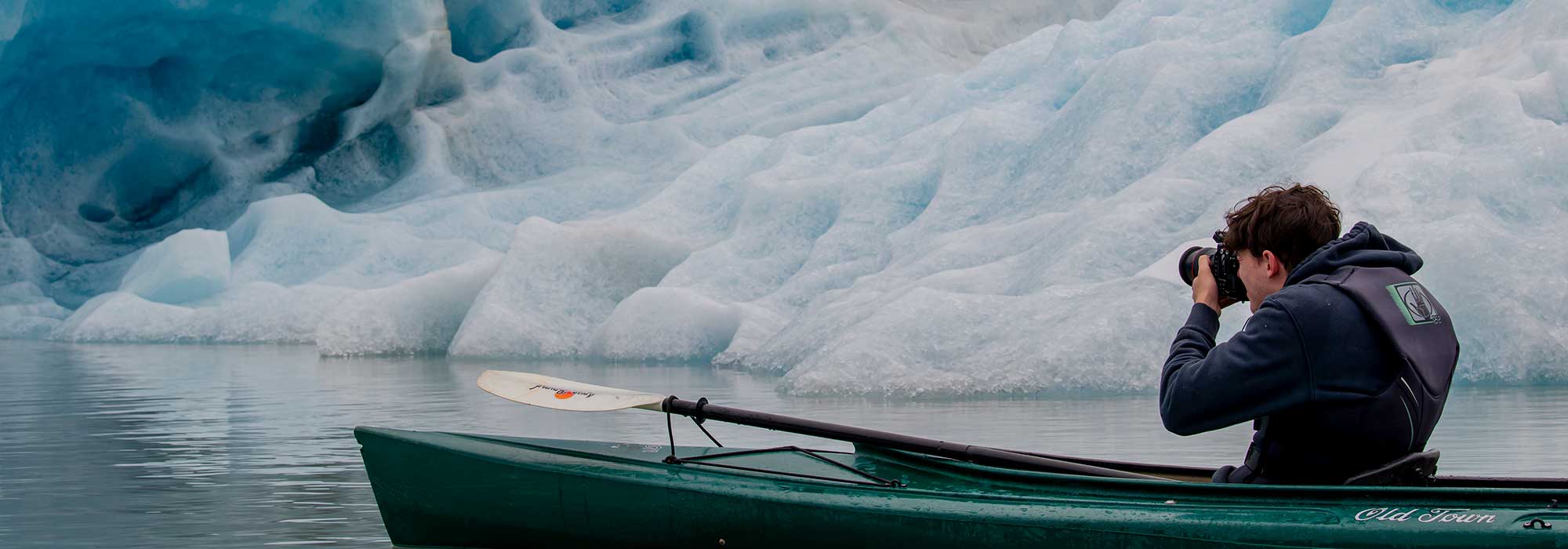 Man in a kayak taking a photo of a glacier