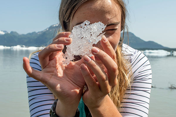 a student holds a small piece of glacier ice in front of their face