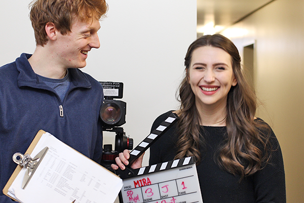 two students filming in Allen Hall with a camera and a slate