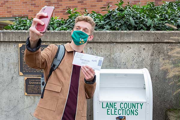 A student taking a selfie with his ballot next to the drop box