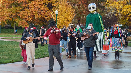 Day of the Dead parade with musicians and people in skeleton costumes.