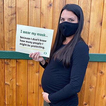A pregnant Abigail Erwin wearing a mask with a sign that says I wear a mask because I don't know how many people I might be protecting.
