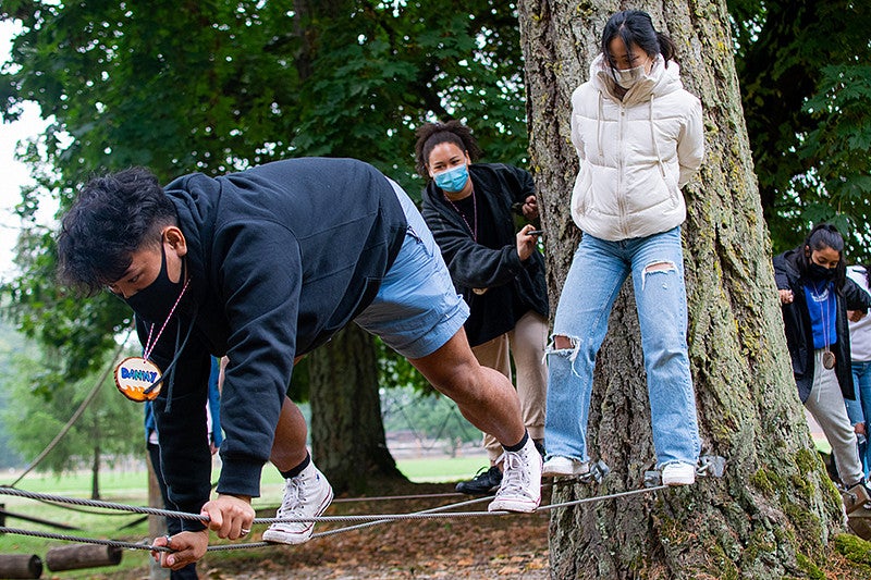a student uses their hands and feet to balance on two ropes on the low ropes course