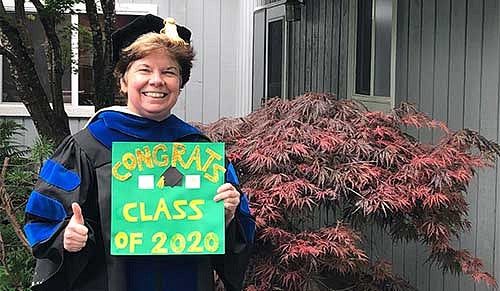 Professor Beth Harn in commencement regalia with a sign that says Congrats Class of 2020