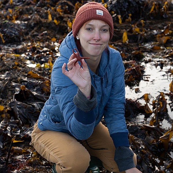 Woman in beanie hat and blue coat holding a maroon sea star.