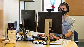 Student wearing a mask and headset sitting at a computer in an office