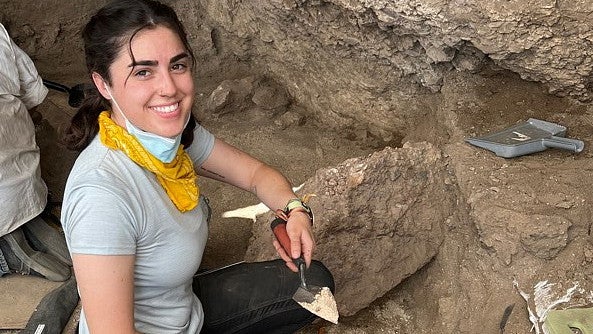 Riley McCormick, a young woman in a gray shirt and yellow kerchief holds a trowel of ash.