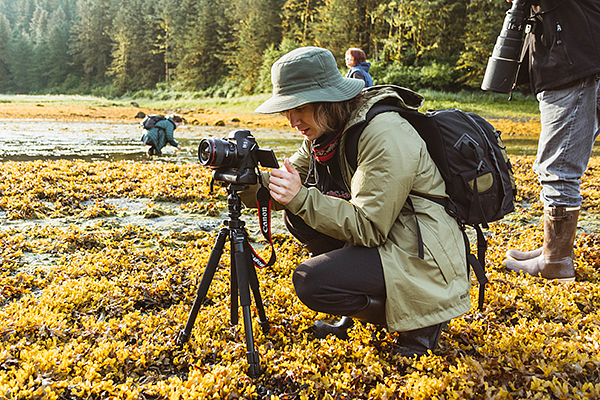 A student crouches behind a camera in a field of golden plants
