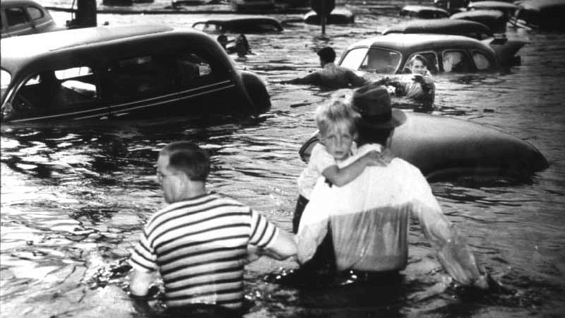 Two men, one carrying a small boy, wading in water up to their waists in Vanport during the flood
