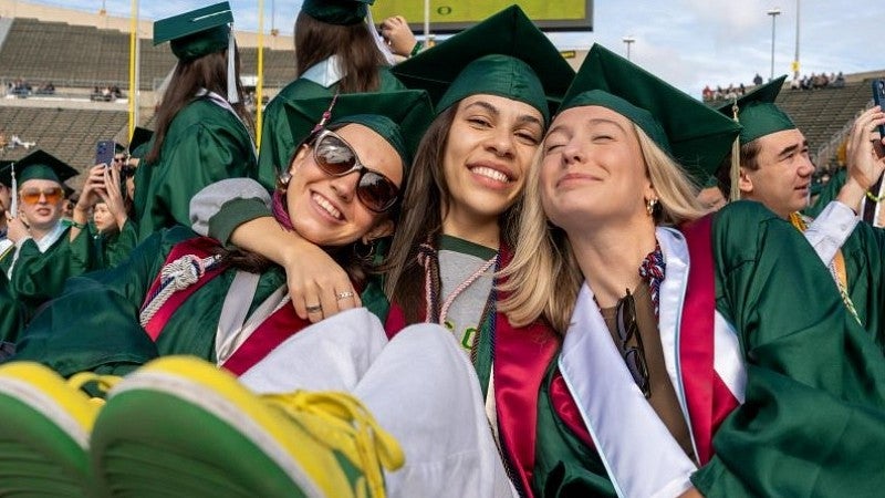 three women grads one has green and yellow sneakers