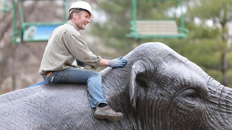 Artist on back of mammoth sculpture