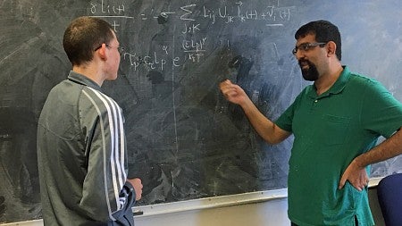 Graduate students Eric Beyerle and Hadi Dinpajooh discuss their work at a blackboard