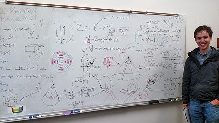 Sean Hixon stands next to a whiteboard where the physics of moving the hats were discussed