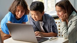 Three kids huddled around laptop