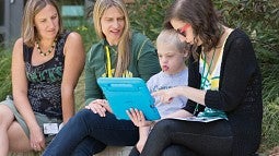 UO faculty sit with a youngster and coach him on a new digital communications tool for developmentally disabled children.