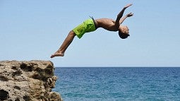 Teenager diving backward off an oceanside cliff
