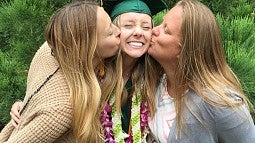 A graduate gets kissed on the cheeks by her sisters. 