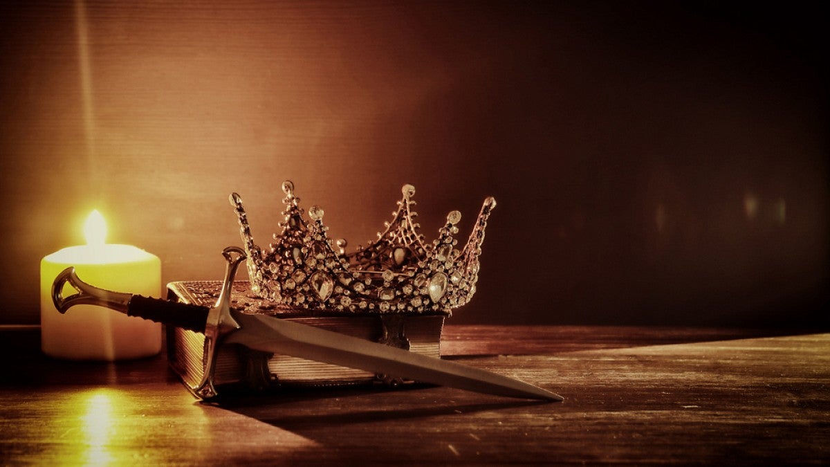 Crown and sword on table lit by candle