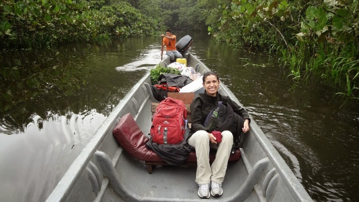 María Belén Noroña traveling upriver in a long canoe through a rainforest.