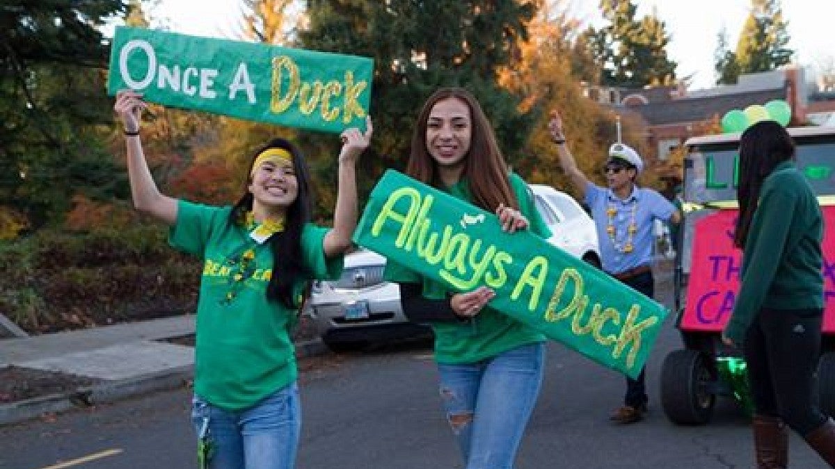 Two students, wearing green, hold signs that say "Once a Duck," "Always a Duck" 