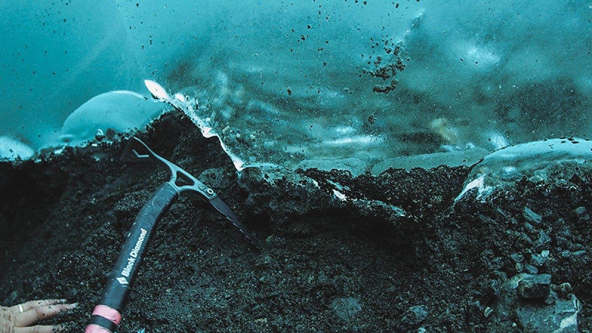 Meyer reaches with an ice axe on frozen sediment beneath a glacier in Alaska